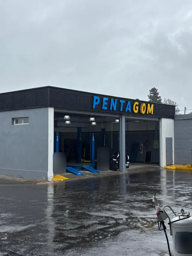 Frente del taller PENTAGOM en un día de lluvia, con el cartel celeste y amarillo